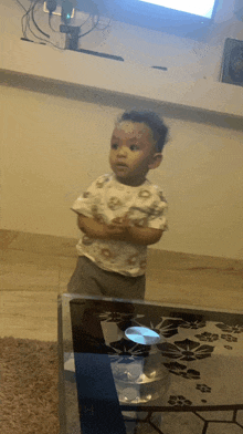 a little boy stands in front of a glass table with his arms crossed