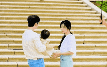 a man and a woman are holding a baby in their arms on a set of stairs .