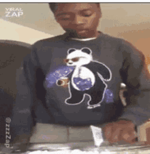 a young man wearing a panda bear sweater is holding a cup of soda .