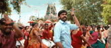 a man in a blue shirt is dancing in front of a crowd of people in front of a temple .