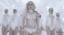 a woman is dancing in a white room with a group of people .