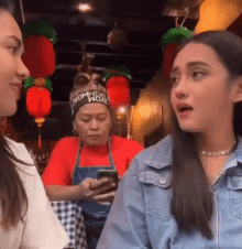 two women are sitting at a table in a restaurant talking to each other . one of the women is holding a cell phone .