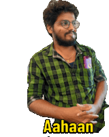 a man wearing glasses and a green plaid shirt has the word aahaan written on his chest