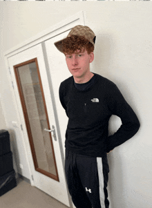 a young man wearing a hat and a sweater that says the north face stands in front of a door