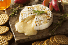 a piece of cheese with a bite taken out of it sits on a wooden cutting board surrounded by crackers