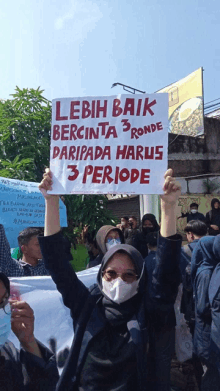 a woman wearing a mask holds up a sign that says lebih baik bercinta 3 ronde