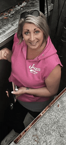 a woman wearing a pink sweatshirt that says jakes on it