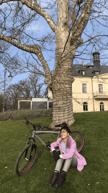 a woman in a pink coat is sitting on the grass next to a bicycle