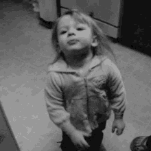 a little girl is standing in a kitchen and making a funny face in a black and white photo .