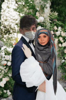 a bride and groom pose for a picture with the bride wearing a hijab and the groom wearing a face mask