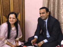 a man in a suit and tie sits next to a woman in a purple sari