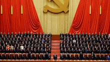 a large group of people standing in front of a red curtain with a hammer and sickle in the background