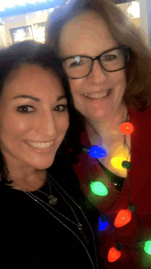 two women are posing for a photo with christmas lights in the background