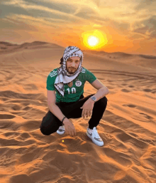 a man wearing a green shirt with the number 10 on it is squatting in the sand