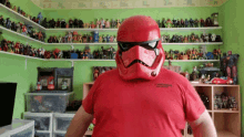 a man wearing a red storm trooper helmet stands in front of a shelf full of action figures and toys