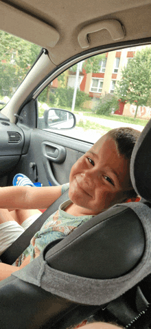 a young boy sits in a car seat smiling at the camera