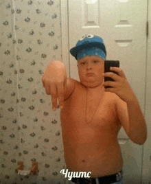 a shirtless boy wearing a cookie monster hat is taking a selfie in a bathroom mirror .