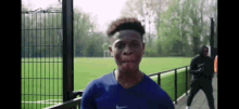 a young man wearing a blue nike shirt is standing in front of a fence on a soccer field .