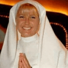 a woman in a white nun costume is smiling and praying .