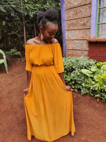 a woman in a yellow off the shoulder dress is standing in front of a brick building