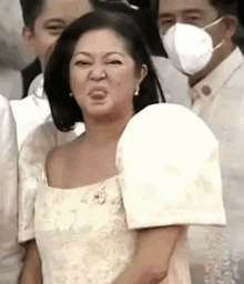 a woman in a white dress is making a funny face in front of a group of people wearing face masks .