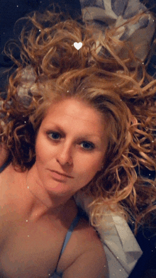 a woman laying on a bed with her hair in the air and a heart in her hair