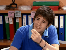 a young man in a blue shirt is sitting at a desk in front of binders with the number 10 on them .