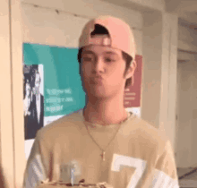 a young man wearing a baseball cap and a necklace is blowing a kiss while holding a cake .