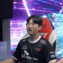 a young man wearing glasses and a sk telecom shirt is sitting in a gaming chair .