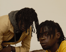 two men with dreadlocks are looking at each other with one wearing a yellow shirt