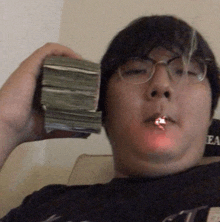 a man wearing glasses is smoking a cigarette while holding a stack of money