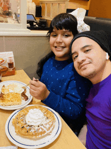 a man and a little girl are sitting at a table with plates of food and a sign that says let 's go breakfast