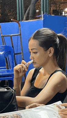 a woman in a black tank top is smoking a cigarette while sitting at a table