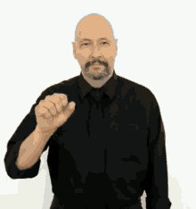 a bald man with a beard and mustache is wearing a black shirt and tie and making a hand gesture .