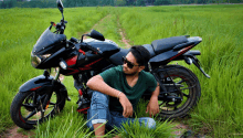 a man sitting in the grass next to a motorcycle that says bajaj pulsar