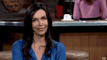 a woman in a blue shirt is smiling in front of a sign that says ' from sea ' on it