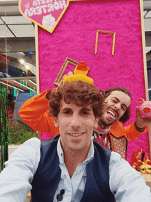 two men are posing for a picture in front of a pink wall with a heart that says ' a' on it