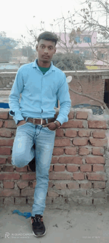 a young man leaning against a brick wall with his leg up