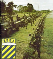 a group of soldiers are standing in a line in a field with a jeep in the background .