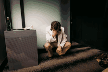 a man in a white jacket is kneeling down with his head in his hands