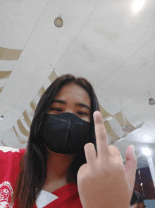 a woman wearing a black mask and a red shirt giving the middle finger