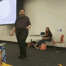 a man in a purple shirt is giving a presentation in front of a projection screen that says " a few words "