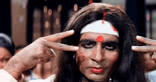 a man with long hair and a bandage on his head is pointing at his forehead