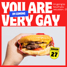 a hand is holding a hamburger in front of a red sign that says you are very gay