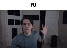 a man in a blue shirt is waving his hand in front of a door with the word ru above him .