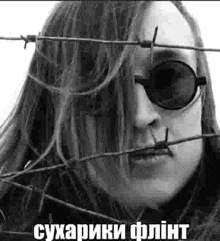 a black and white photo of a woman wearing sunglasses and barbed wire around her face .