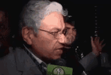 a man wearing glasses is talking into a green microphone