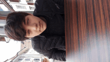 a young man wearing a black jacket with the word columbia on it sits at a table