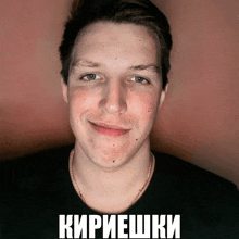 a man wearing a black shirt and a gold chain smiles in front of a sign that says ' киришки ' on it