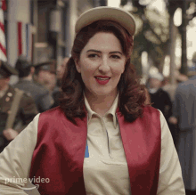 a woman wearing a red vest and a white shirt is standing in front of a crowd of people and a sign that says prime video